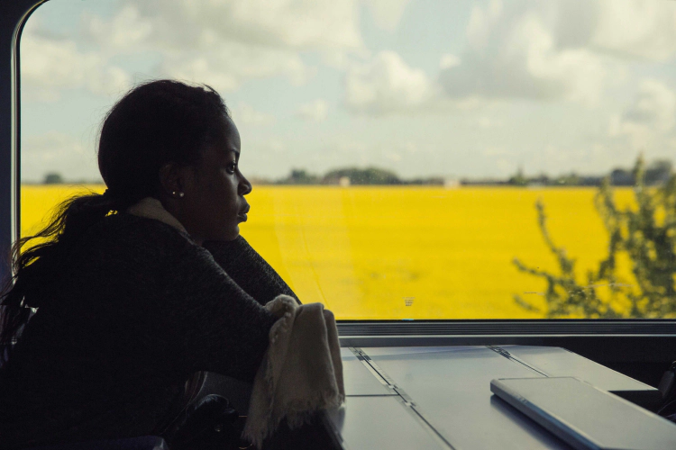 A woman of color sits in a train looking ahead and pondering.